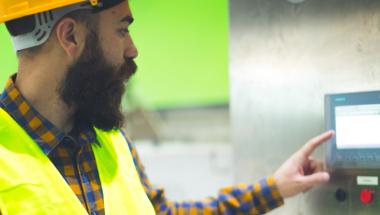 Man wearing hardhat touching equipment control screen 