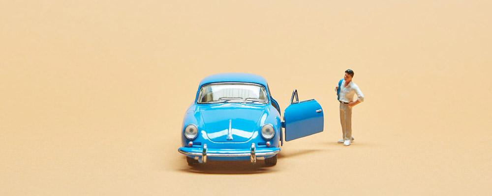 Man standing next to small blue car